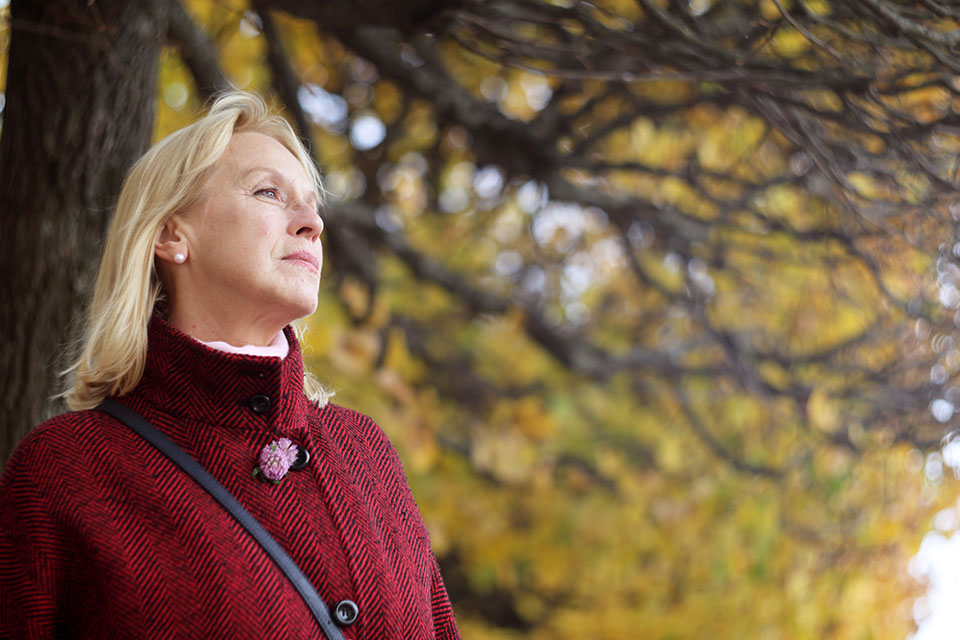 Senior woman in autumn park over yellow tree background